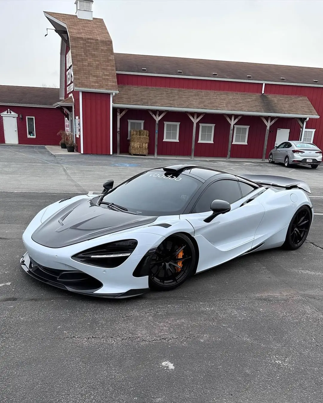 White and black McLaren 720S sports car parked in front of a red barn-like building.