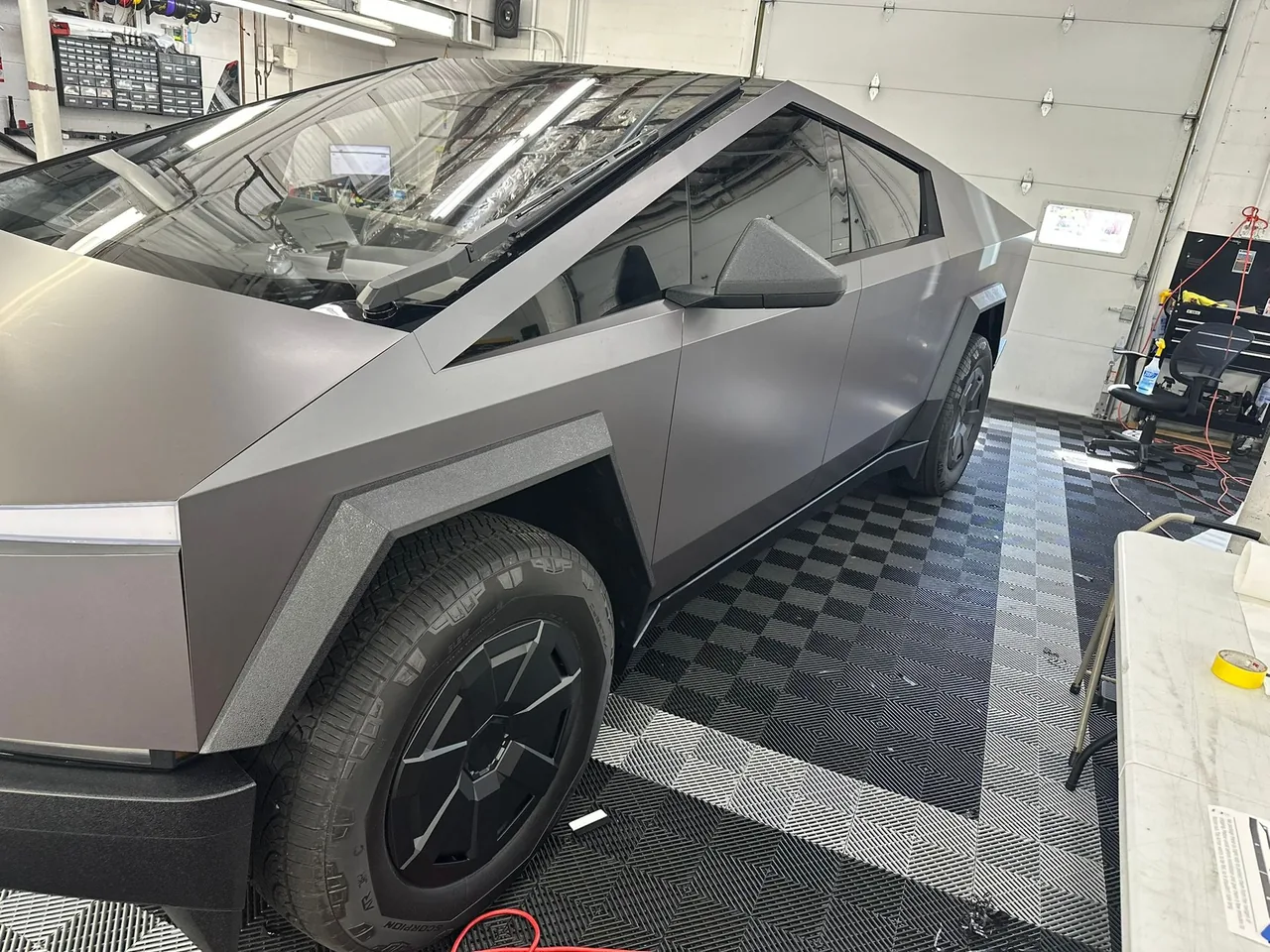 Gray Tesla Cybertruck in a garage, matte finish, angled view.