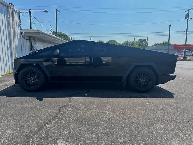 Black Tesla Cybertruck parked on asphalt near a building, with tinted windows and dark wheels.