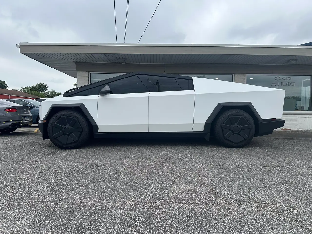 White Tesla Cybertruck parked on gravel. Black tires, tinted windows. Cloudy day.