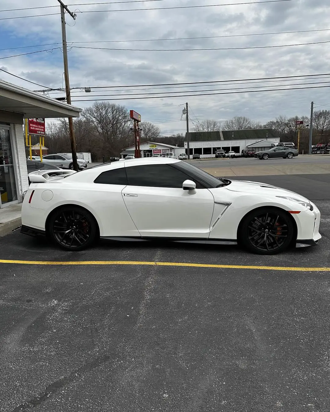 White Nissan GT-R parked on asphalt next to a storefront under a cloudy sky.