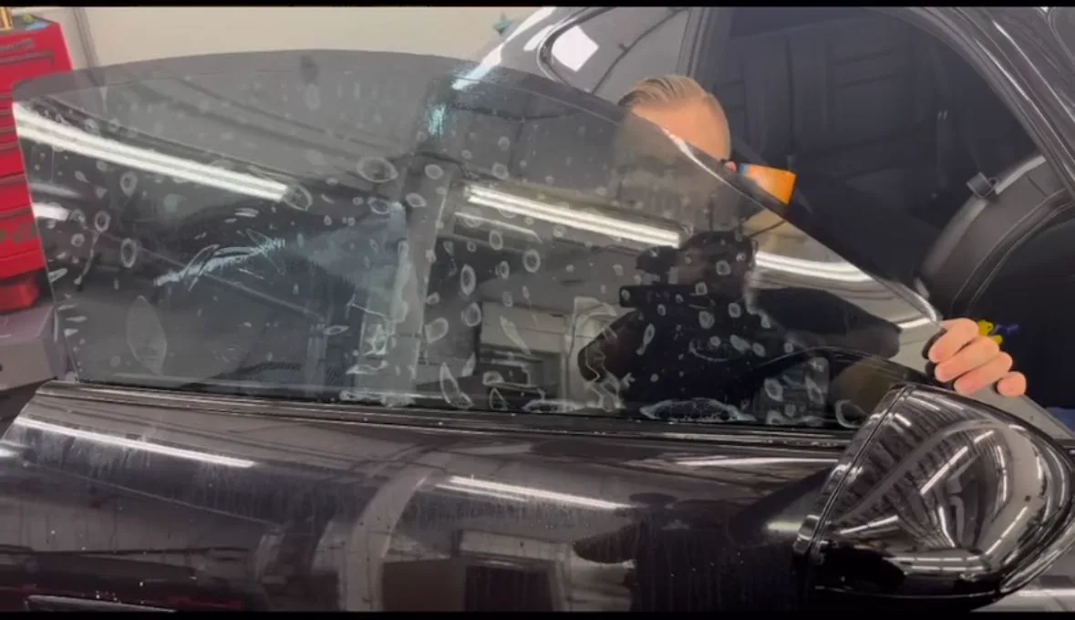 Person applying tint to a car window in a garage.